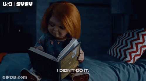 A Baby Doll Is Sitting On A Bed Reading A Book . GIF