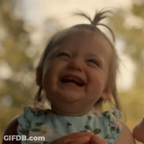 A Baby Girl In A Blue Dress Is Laughing With Her Mouth Open GIF