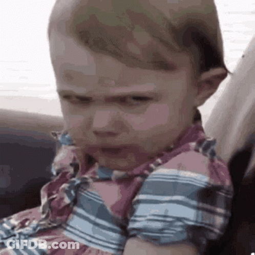 A Baby Girl Is Making A Funny Face While Sitting On A Couch . GIF