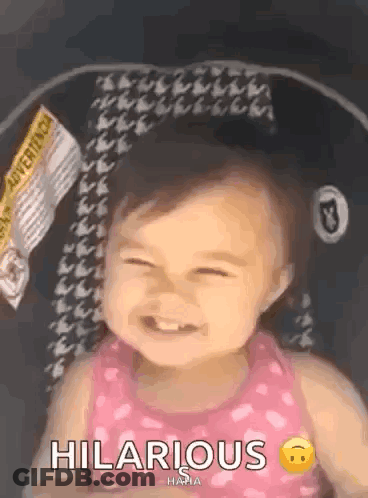 A Baby Girl Is Sitting In A Car Seat And Smiling With The Words Hilarious Written Next To Her . GIF