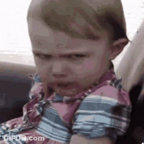 A Baby Girl Is Sitting In A Car Seat With A Serious Look On Her Face . GIF