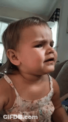 A Baby Girl Is Sitting On A Couch And Crying . GIF