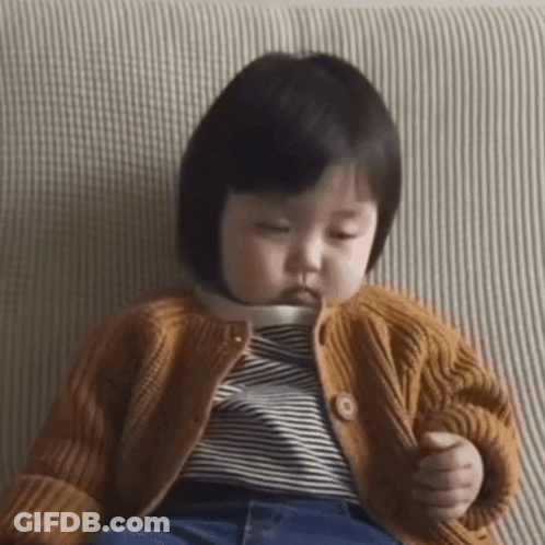 A Baby Girl Is Sitting On A Couch Wearing A Sweater And Striped Shirt . GIF