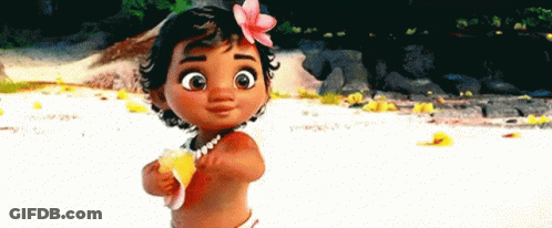 A Baby Girl With A Flower In Her Hair Is Standing On A Beach Holding A Shell . GIF