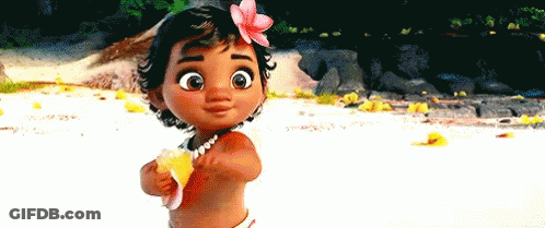 A Baby Girl With A Flower In Her Hair Is Standing On A Beach Holding A Shell . GIF