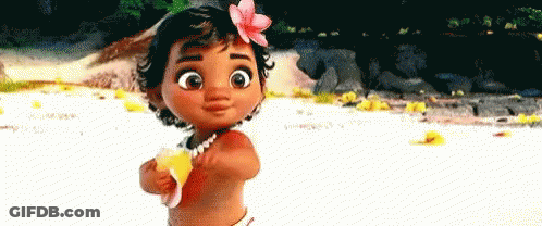 A Baby Girl With A Flower In Her Hair Is Standing On The Beach Holding A Banana . GIF