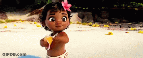 A Baby Girl With A Flower In Her Hair Is Standing On The Beach Holding A Shell . GIF