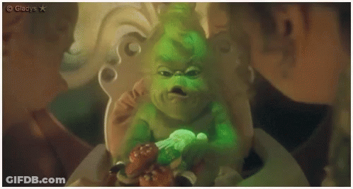 A Baby Grinch Is Sitting In A High Chair With A Candy Cane . GIF