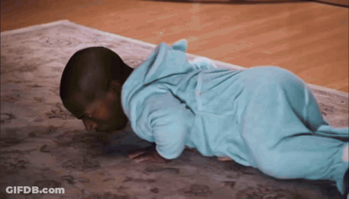 A Baby In A Blue Pajamas Is Doing Push Ups On A Rug GIF
