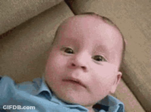 A Baby In A Blue Shirt Is Laying On A Couch And Making A Funny Face . GIF