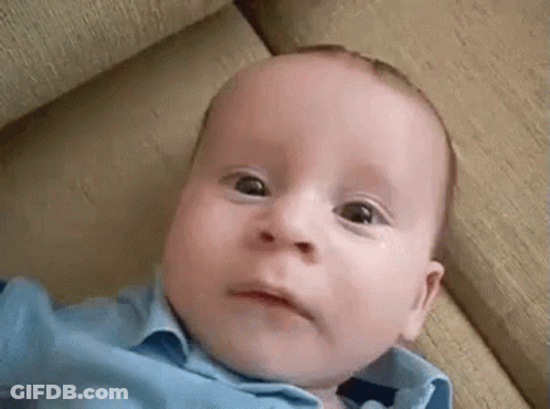 A Baby In A Blue Shirt Is Laying On A Couch Making A Funny Face . GIF