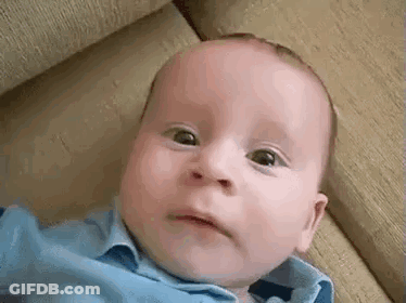 A Baby In A Blue Shirt Is Laying On A Couch Making A Funny Face . GIF