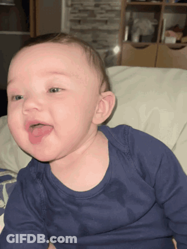 A Baby In A Blue Shirt Is Sticking Out Its Tongue GIF