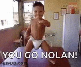 A Baby In A Diaper Is Pointing At The Camera While Standing On A Purple Balloon . GIF