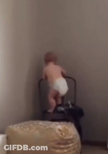 A Baby In A Diaper Is Standing Next To A Chair . GIF