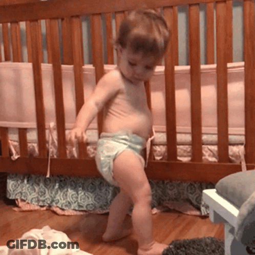 A Baby In A Diaper Is Standing Next To A Crib GIF
