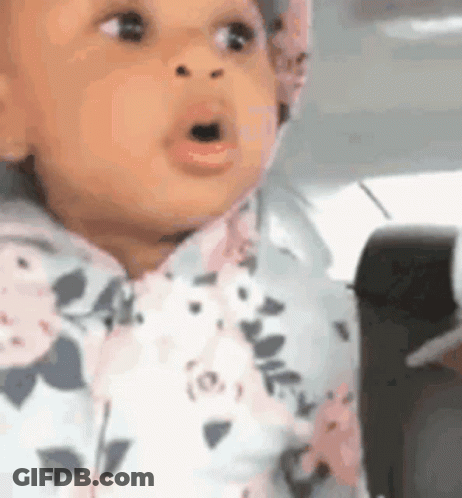 A Baby In A Floral Outfit Is Sitting In A Car Seat With Her Mouth Open . GIF