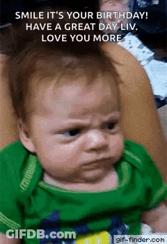 A Baby In A Green Shirt Is Making A Funny Face While Being Held By A Woman . GIF