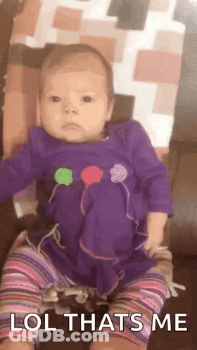 A Baby In A Purple Dress Is Sitting On A Couch And Making A Face . GIF