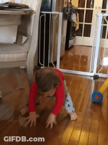 A Baby In A Red Shirt Is Crawling On The Floor In Front Of A White Gate GIF