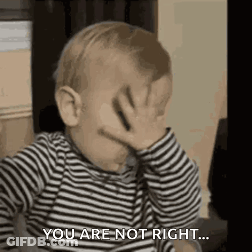 A Baby In A Striped Shirt Is Covering His Face With His Hand . GIF