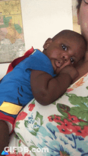 A Baby In A Superman Costume Is Being Held By A Woman In A Momento Photo GIF