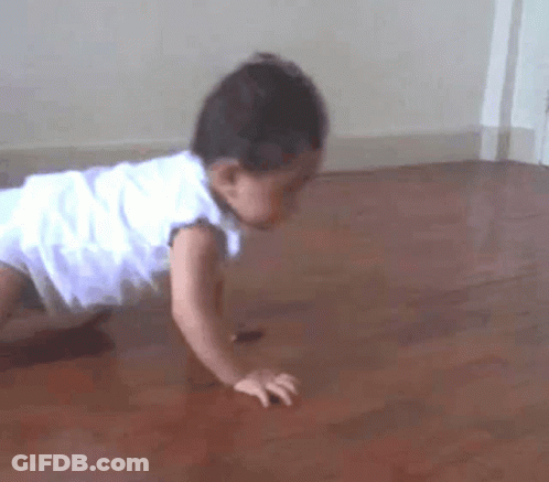 A Baby In A White Dress Is Crawling On A Wooden Floor . GIF