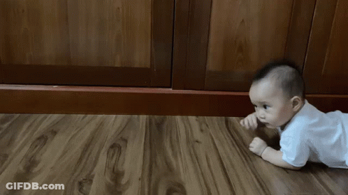 A Baby In A White Shirt Is Crawling On A Wood Floor GIF
