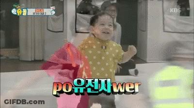 A Baby In A Yellow Polka Dot Shirt Stands In Front Of A Kbs Logo GIF