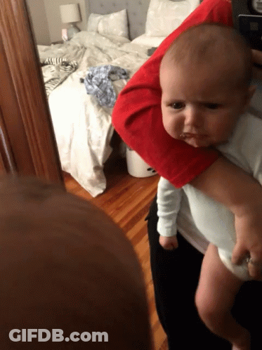 A Baby Is Being Held By A Person In Front Of A Messy Bed GIF