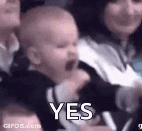 A Baby Is Being Held By A Woman In A Crowd And Making A Funny Face . GIF
