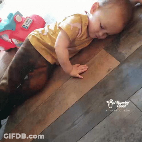 A Baby Is Crawling On A Wooden Floor Next To A Toy Car With The Number 2123 On It GIF