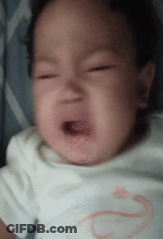 A Baby Is Crying With His Mouth Open And A White Shirt On . GIF