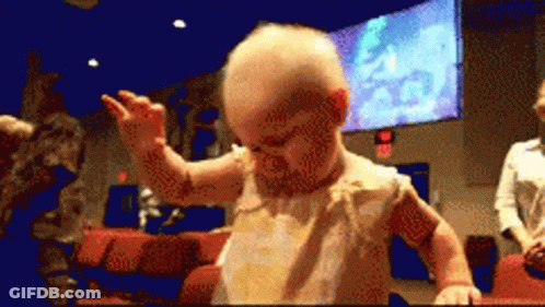 A Baby Is Dancing In Front Of A Large Screen That Says Exit GIF