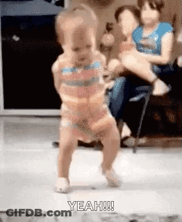 A Baby Is Dancing On The Floor In A Living Room While A Woman Holds Her . GIF