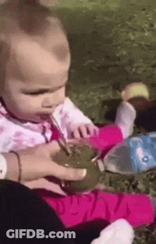A Baby Is Drinking From A Cup With A Spoon GIF