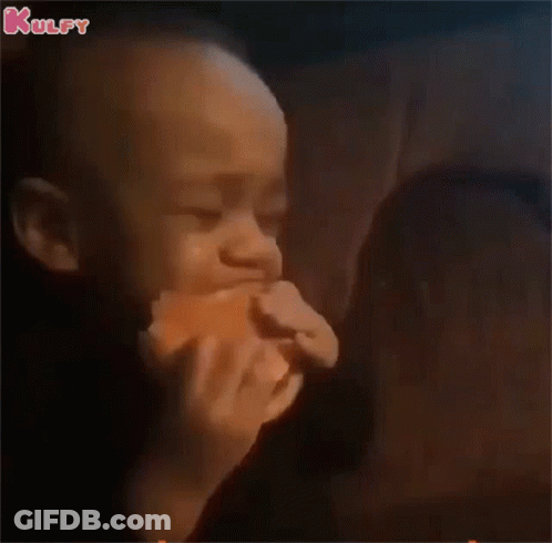 A Baby Is Eating A Hamburger In A Dark Room While A Woman Looks On . GIF