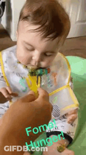 A Baby Is Eating Broccoli With A Fork And Bib On . GIF