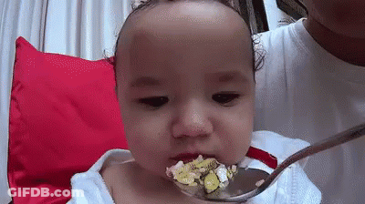 A Baby Is Eating From A Spoon With A Spoon In His Mouth . GIF