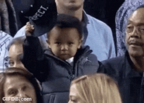 A Baby Is Holding A Hat In A Crowd Of People At A Basketball Game . GIF