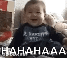 A Baby Is Laughing While Sitting On A Bed With Boxes . GIF