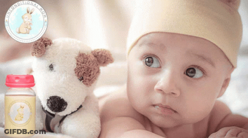 A Baby Is Laying Next To A Stuffed Dog And A Bottle Of Breast Milk GIF