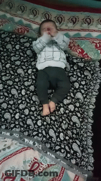 A Baby Is Laying On A Bed With A Paisley Patterned Blanket GIF