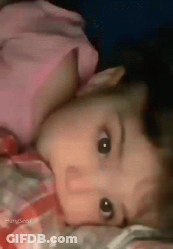 A Baby Is Laying On A Bed With His Head On A Pillow And Looking At The Camera . GIF