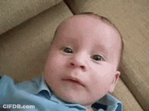 A Baby Is Laying On A Couch And Looking At The Camera . GIF