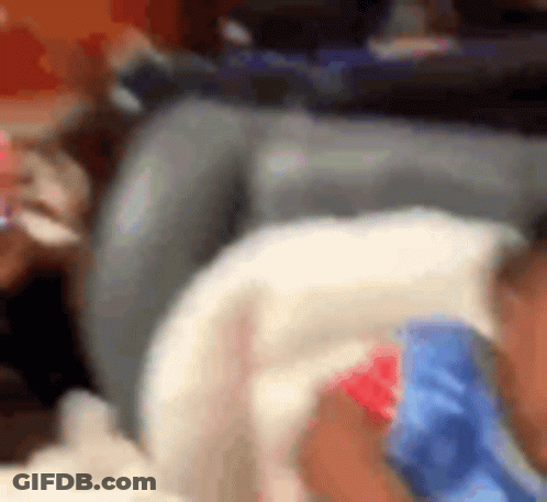 A Baby Is Laying On A Couch Wearing A Blue And Red Shirt . GIF