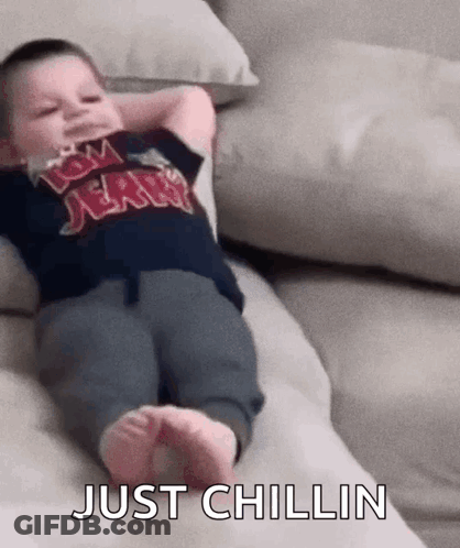 A Baby Is Laying On A Couch With His Arms Over His Head And The Words `` Just Chillin '' Written On The Bottom . GIF