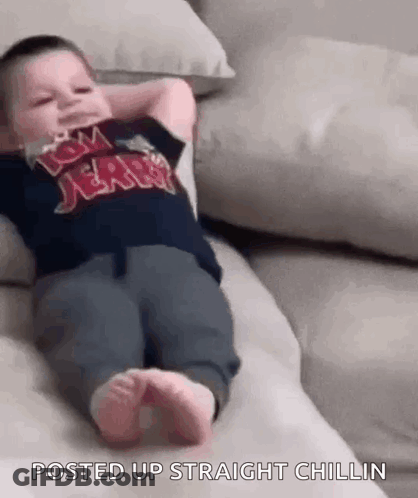 A Baby Is Laying On A Couch With His Hands Behind His Head And His Feet Up . GIF