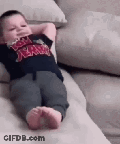 A Baby Is Laying On A Couch With His Hands Behind His Head And Wearing A Tom And Jerry Shirt . GIF
