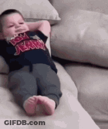 A Baby Is Laying On A Couch With His Hands Behind His Head And Wearing A Tom Jerry Shirt . GIF